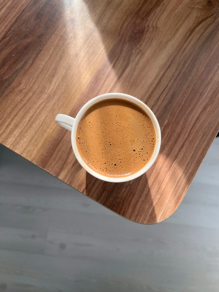 Overhead shot of a coffee cup on a wooden table with natural sunlight.